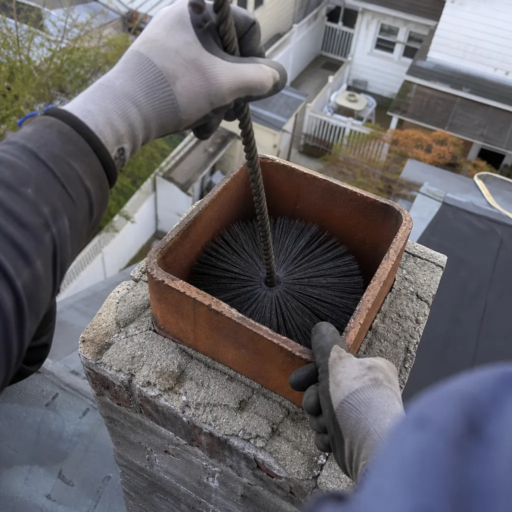 Professional chimney sweep cleaning a residential brick chimney on a roof